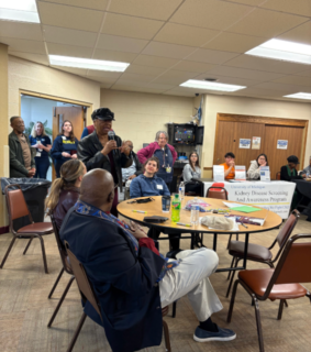 A community health fair with tables displaying Hope Clinic and Cancer Support Community materials. Attendees engage, creating an informative atmosphere.