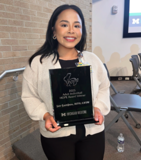 Smiling woman holding a "2025 Adult Individual HOPE Award" plaque from Michigan Medicine, standing in a lecture hall setting.