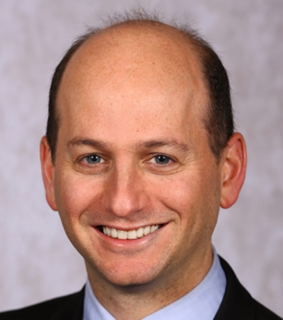 A man in a suit and tie, smiling cheerfully, conveying a professional demeanor.