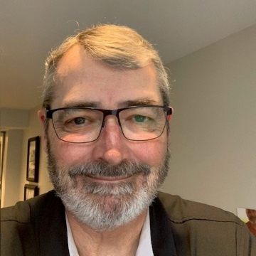 A man with a beard and glasses smiles warmly