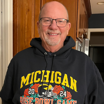 A man in a Michigan hoodie smiles.