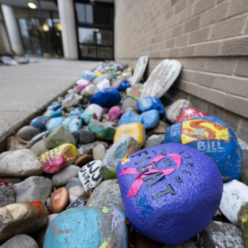 Painted rocks with inspirational messages like "Hope" and colorful designs line the ground outside Michigan Medicine Radiation Oncology building, conveying positivity and encouragement.