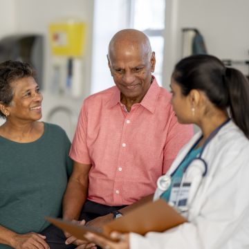 A doctor consults with an older couple in a medical office. The couple looks attentive and engaged, conveying a positive and trusting atmosphere.