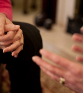 Close-up of two people having an intimate conversation. One person gestures while the other clasps their own hands, creating a warm, empathetic atmosphere.